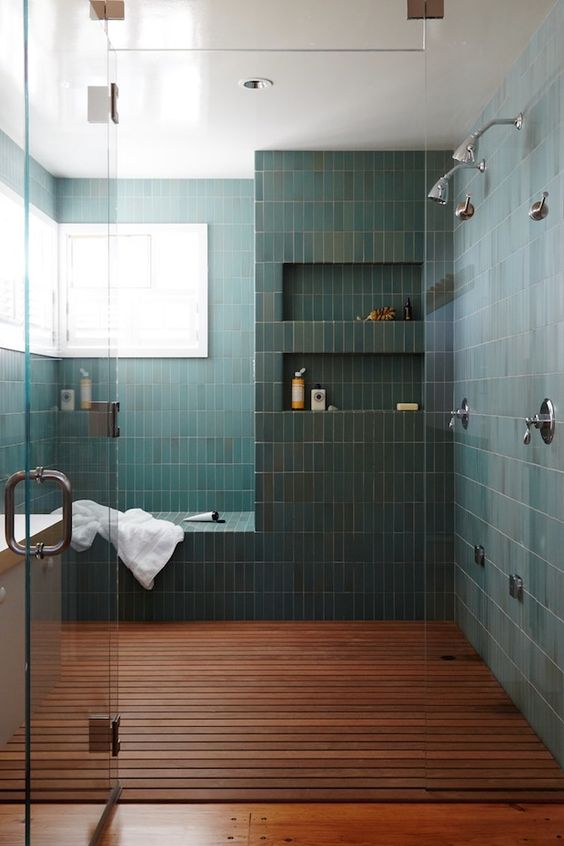 a chic bathroom with a large shower space clad with green stacked tiles, with a bench and niches in the walls, a dark-stained floor and windows for natural light