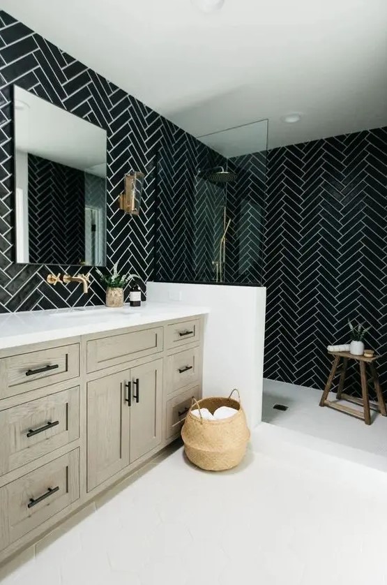 a chic black and white bathroom with chevron tiles, a greige wooden vanity, black fixtures and a wooden stool plus a basket for storage is cool