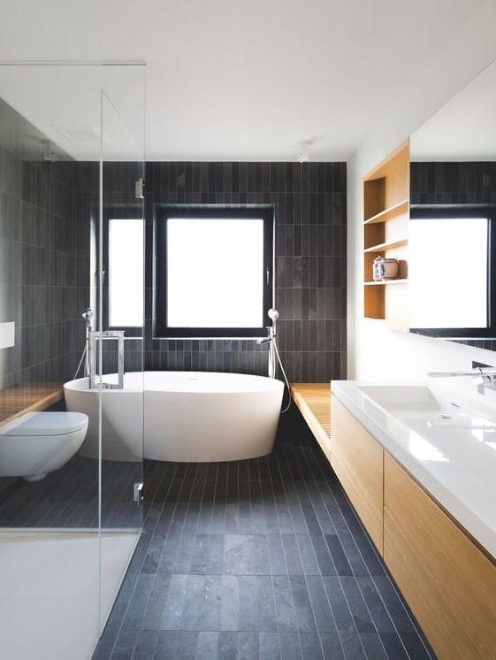a contemporary bathroom all clad with matte dark skinny tiles and refreshed with light colored wood and white pieces
