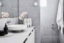 a contemporary bathroom clad with grey terrazzo tiles, with a white vanity, a marble countertop, a round sink, a cool vase and orchids
