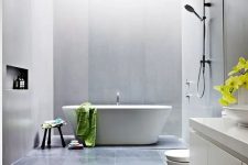 a contemporary bathroom with black and grey large scale tiles, a tub, a floating white vanity, white appliances and neutral fixtures