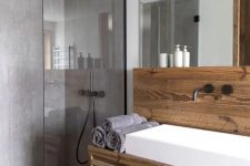 a contemporary chalet bathroom clad with wood and with lots of concrete in decor, with a large mirror, a white sink and a rainshower