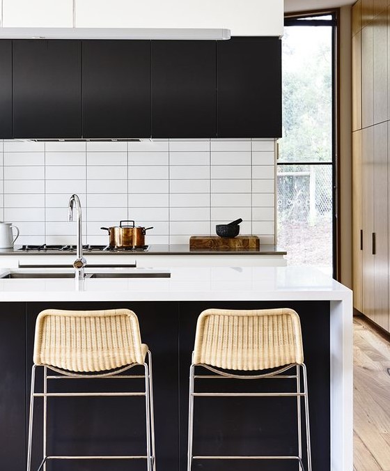 a contrasting contemporary kitchen with black cabinets, white stone countertops and a white stacked tile backsplash