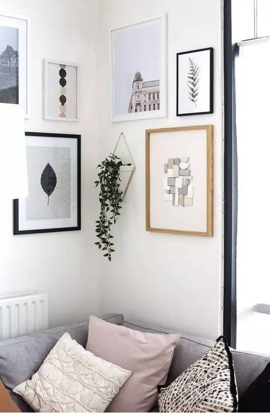 a cool modern gallery wall with mismatching white, black and neutral frames and various types of art plus hanging greenery