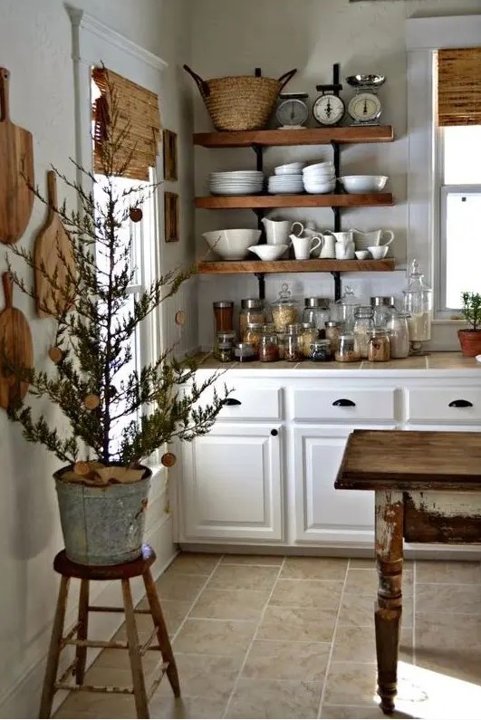 a country cottage kitchen with white cabinets, open shelves, cutting boards on the wall, a shabby chic kitchen island that is a table