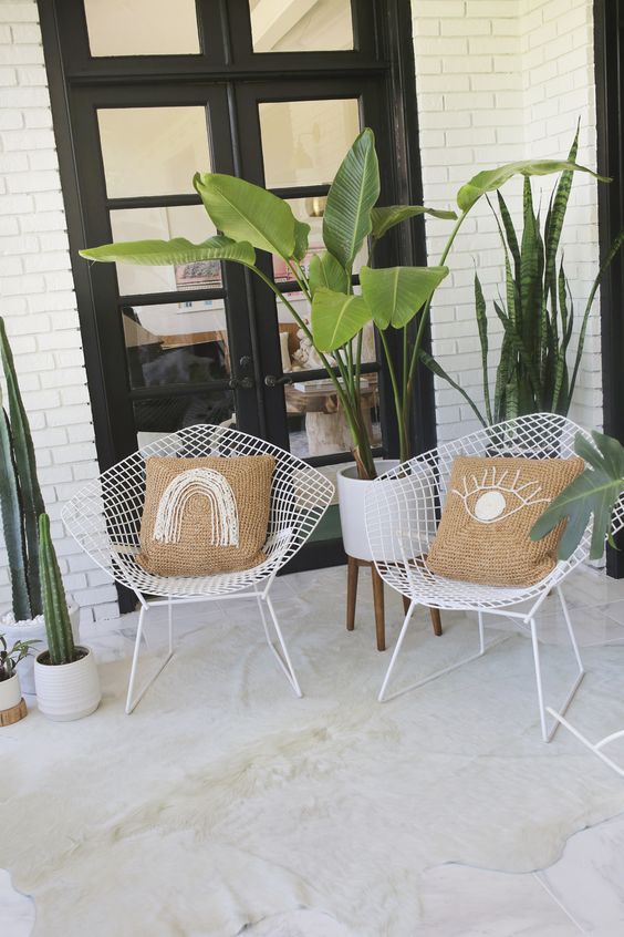 a cozy outdoor nook with potted plants and cacti, a couple of white metal chairs with embroidered pillows looks welcoming