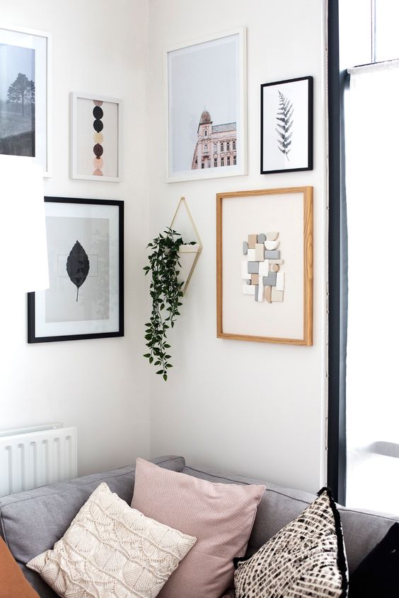 a dreamy neutral corner gallery wall with prints, artwork and even an applique plus a potted plant in a hanging planter is awesome