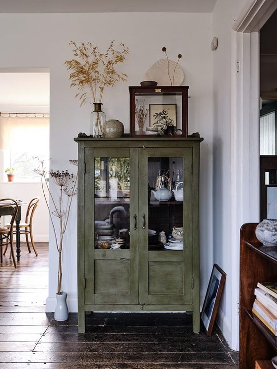 a green shabby chic cabinet with glass doors is used for storing tableware and porcelain in a rustic dining room or kitchen