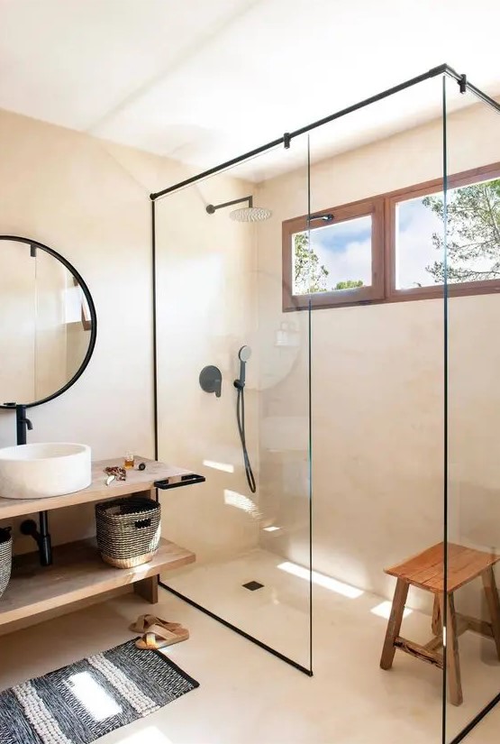 a greige contemporary bathroom with a shower space enclosed in glass, a floating open shelf vanity, a round mirror in a black frame, black fixtures