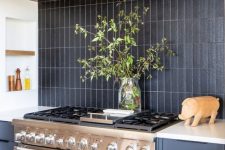 a grey kitchen with wooden beams, a black matte stacked tile backsplash and a metal cooker and hood