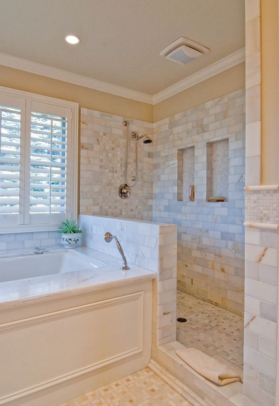 a lovely bathroom clad with marble tiles, with a half wall in the shower space, a bathtub clad with panels