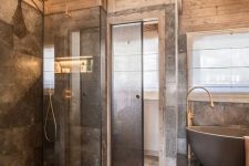 a luxurious chalet bathroom done with grey marble and light-stained wood, with brass touches and a bathtub on a platform