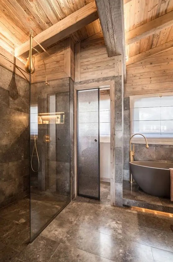 a luxurious chalet bathroom done with grey marble and light stained wood, with brass touches and a bathtub on a platform