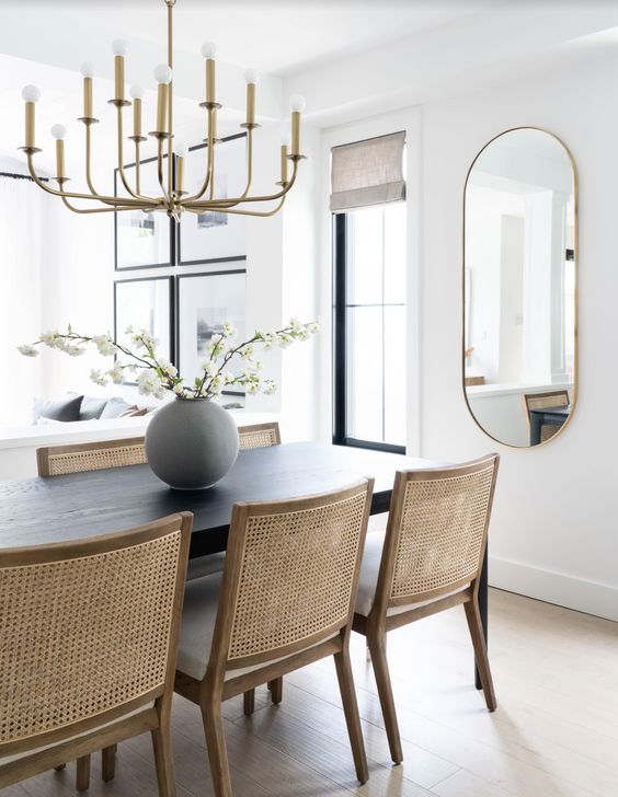 a mid-century modern dining space with a dark-stained table and neutral chairs with cane backs and a chic chandelier plus an oval mirror