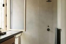 a minimalist bathroom clad with light stained wood and with concrete, with black fixtures and a vanitu with a concrete countertop