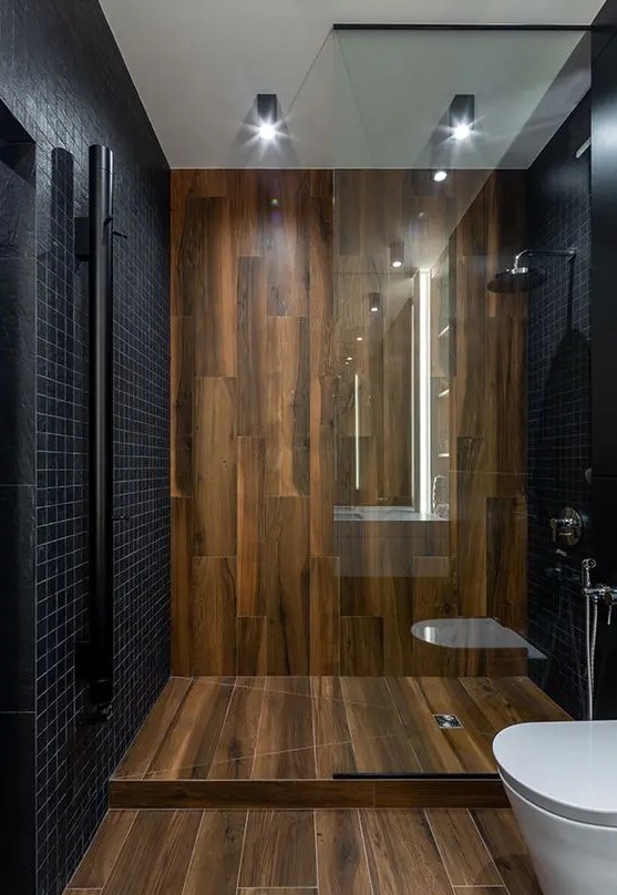 a minimalist bathroom clad with small black tiles and with wood like tiles for a super elegant and contrasting look