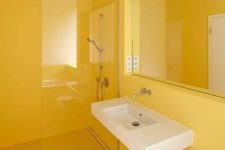 a minimalist sunny yellow bathroom done sleek and plain, with a statement mirror and a floating sink