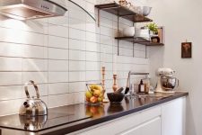 a minimalist white kitchen with a white stacked tile wall, black countertops and shelves is very chic