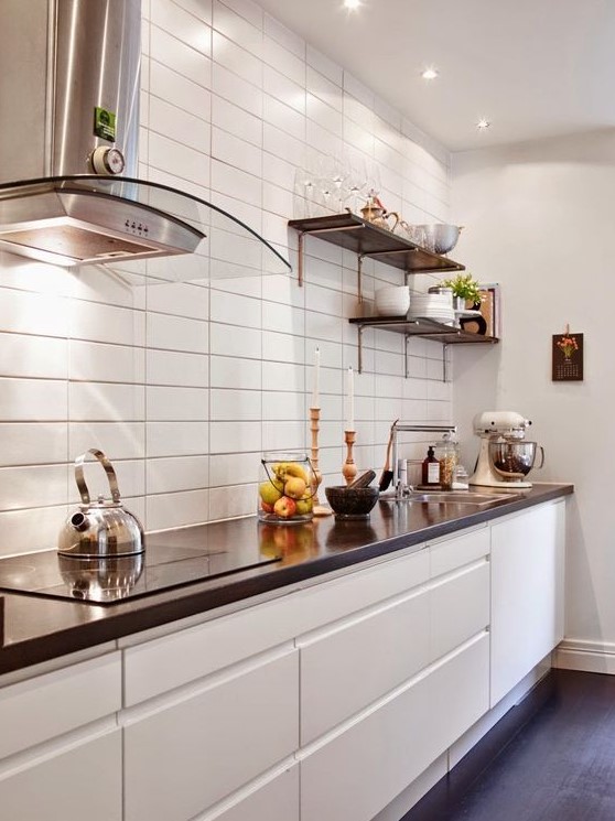 a minimalist white kitchen with a white stacked tile wall, black countertops and shelves is very chic