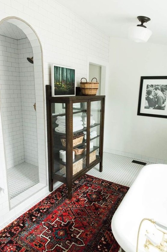 a modern bathroom with a bright rug, white tiles all over and a vintage dark stained glass armoire