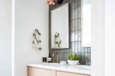 a modern bathroom with grey stacked skinny tiles, a blonde wood vanity with a white countertop, brass fixtures and copper sconces