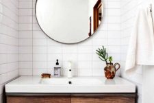 a modern farmhouse bathroom with stacked white tiles, a dark-stained built-in vanity and a round mirror is all cool