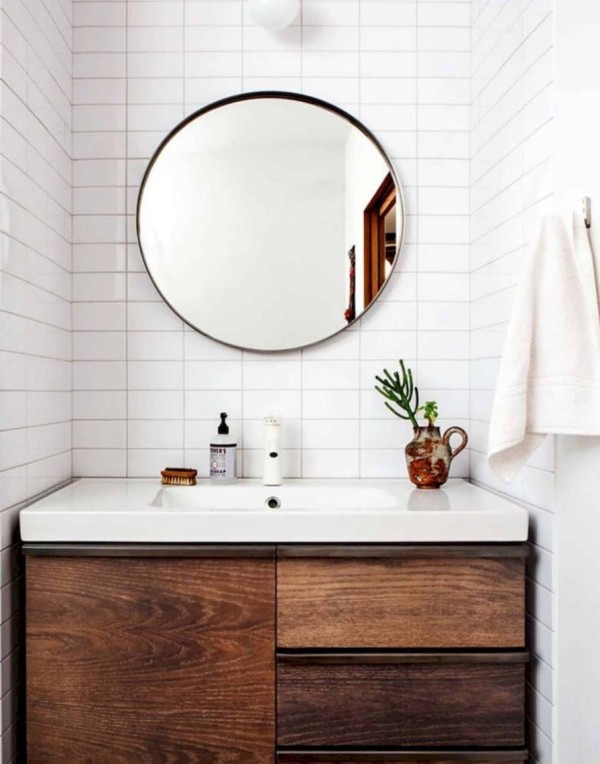 a modern farmhouse bathroom with stacked white tiles, a dark-stained built-in vanity and a round mirror is all cool
