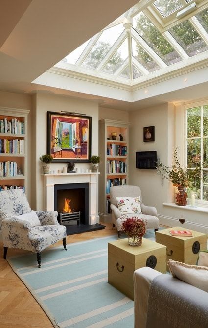a modern neutral living room with a glass roof, a fireplace, built-in bookshelves, a neutral sofa, yellow chests and vintage chairs