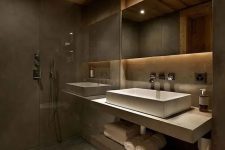 a moody chalet bathroom done with concrete and textural wood, with a floating vanity and a white sink, a lit up mirror