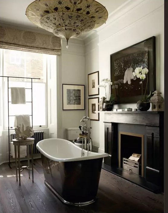 a moody vintage bathroom with a vintage fireplace, a black bathtub, a gallery wall and printed curtains and a printed pendant lamp