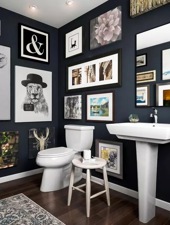 a navy bathroom with a gallery wall that takes all the blank wall space, white appliances and a mirror integrated into this art spot