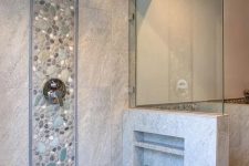 a neutral bathroom clad with tiles and faux pebbles, with a pony wall that had some shelves integrated is a lovely space