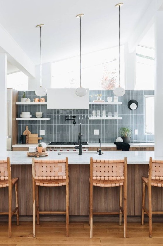 a neutral stained wooden kitchen, white shelves and a hood, a blue stacked tile wall and pendant lamps