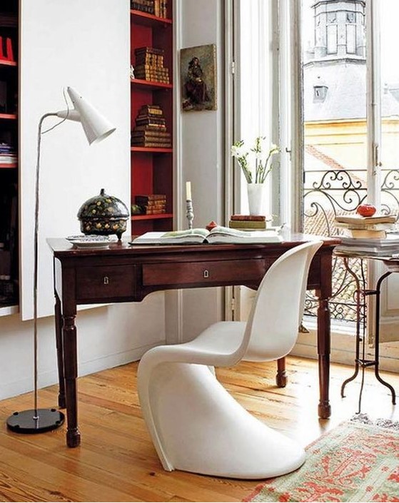 a refined contemporary home office with built-in bookshelves, a vintage stained desk, a white sculptural chair and a small table