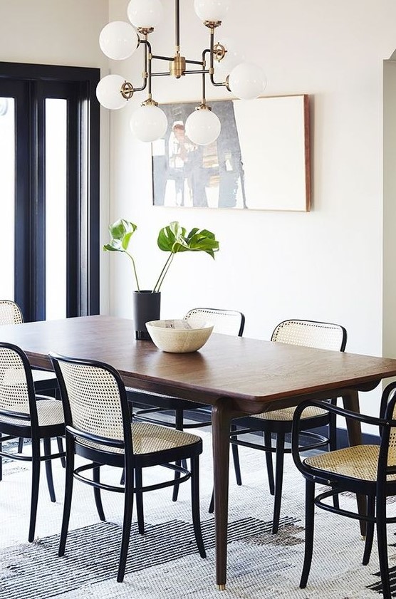 a refined modern dining room with a stained table, black chairs with cane backs and seats, a vintage chandelier and a statement artwork