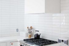 a serene white kitchen with a white stacked tile backsplash, copper fixtures and a white hood is very welcoming