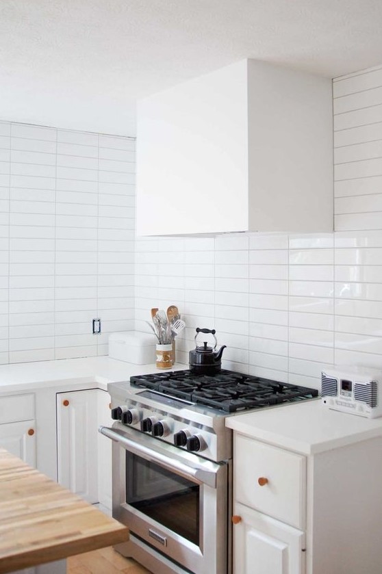a serene white kitchen with a white stacked tile backsplash, copper fixtures and a white hood is very welcoming
