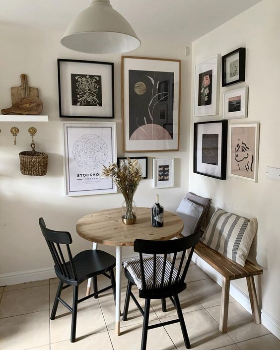 a small and cool dining space with a floating bench, a stained table, black chairs and a catchy corner gallery wall plus a pendant lamp