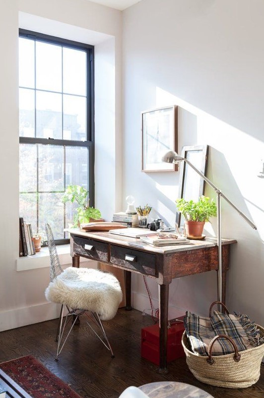 a small and cozy workspace with a dark stained desk, a metal chair, potted plants and pretty artworks plus a floor lamp