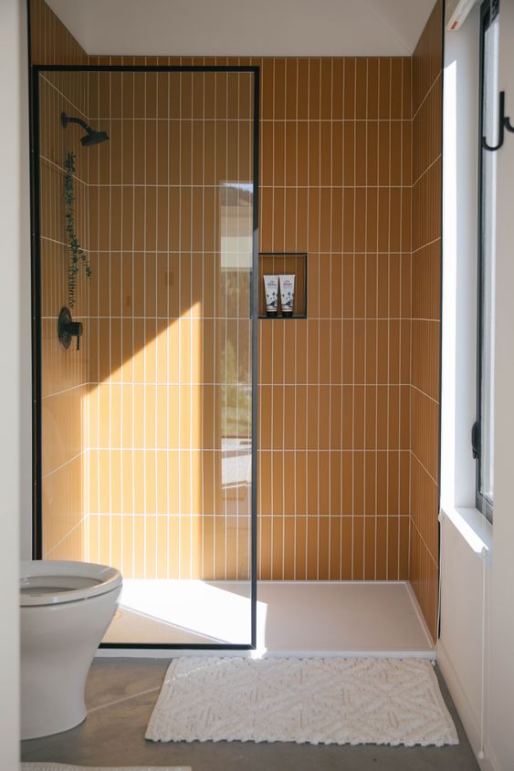 a small contemporary bathroom with stacked yellow skinny tiles in the shower, white appliances and a window for natural light