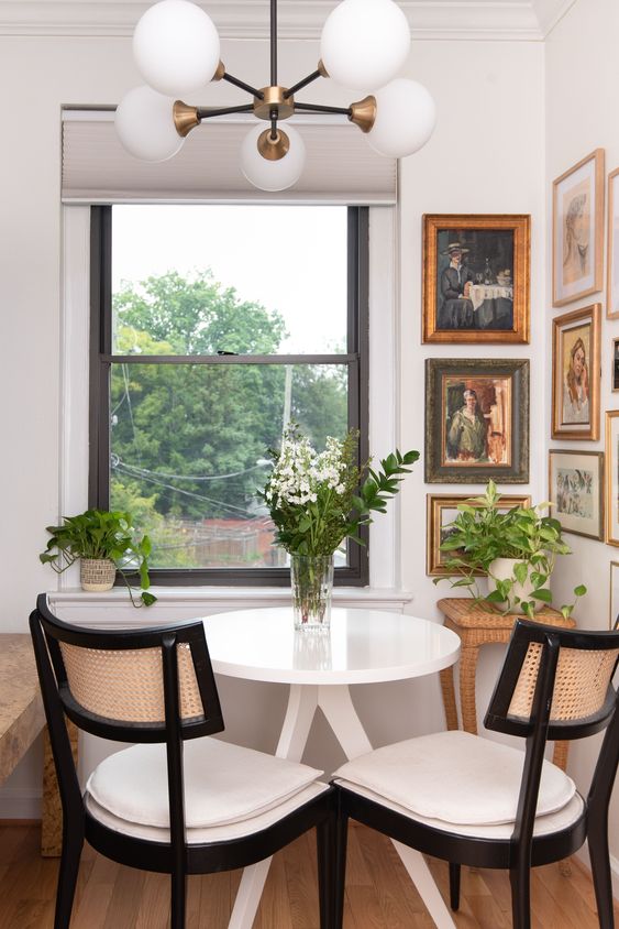 a small vintage dining space with a beautiful vintage corner gallery wall, a white table, neutral chairs, greenery and blooms and a stylish chandelier