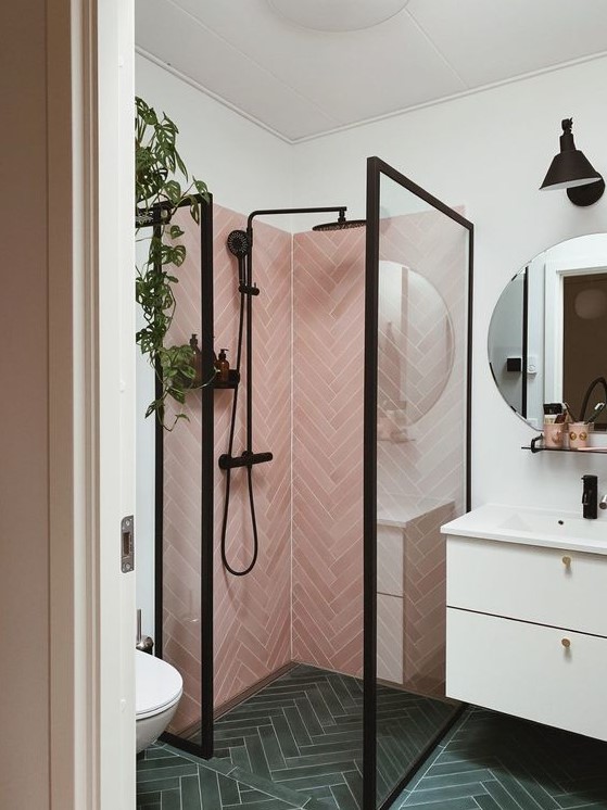 a small yet catchy bathroom with pink herringbone tiles and green ones, a white vanity and black fixtures here and there