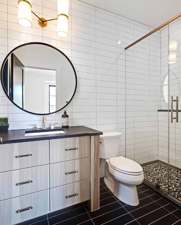 a stylish modern bathroom with white and black skinny tiles clad stacked, a timber vanity, a round mirror and a sconce