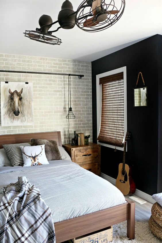 a stylish teen bedroom with a black accent wall and a brick one, a wooden bed and nightstands, neutral textiles, fans and a pendant lamp of metal