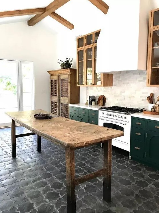 a stylish two-tone kitchen with a large hood, wooden beams on the ceiling, a tiled floor and a vintage wooden table