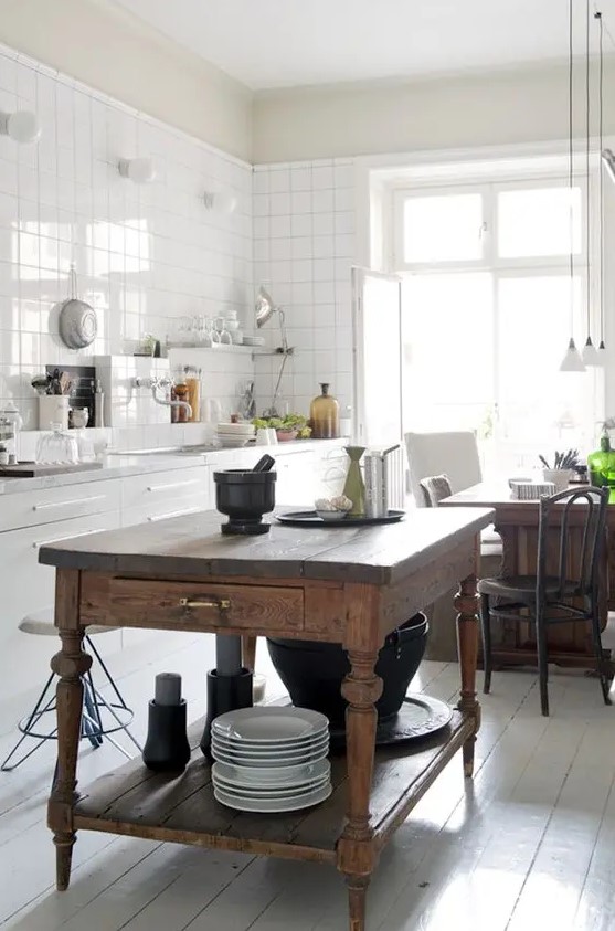 a white Scandinavian kitchen with white square tiles on the walls, a vintage stained kitchen island and a table in one, pendant lamps