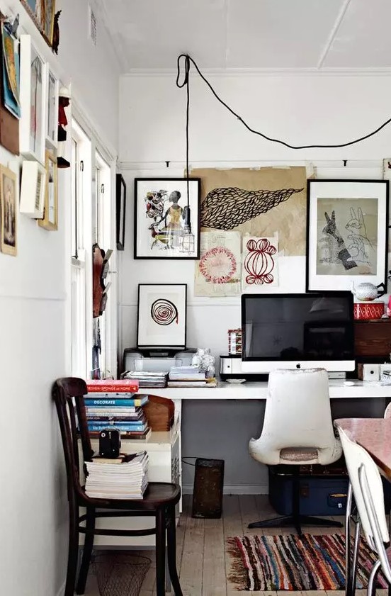 an eclectic home office wiht a white desk and a creamy chair, with a messy gallery wall that extends to the next wall, some chairs and a bold rug
