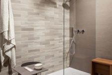an elegant bathroom with taupe tiles on the walls, a chevron floor, neutral tiles for an accent wall, a taupe table and a wooden stool