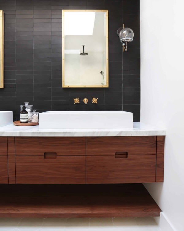 an elegant modern farmhouse bathroom with black skinny stacked tiles, a dark-stained timber vanity and mirrors in gold frames, two sinks