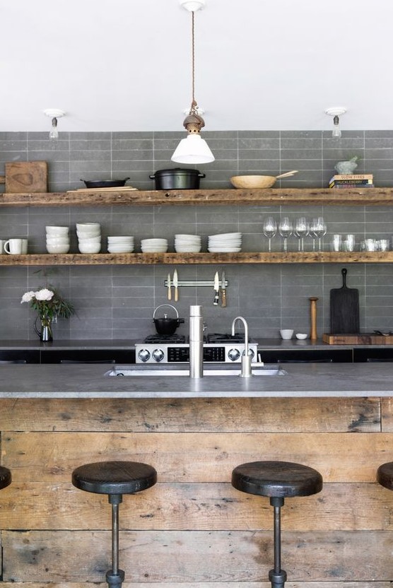 an industrial kitchen with matte grey stacked tiles, rough wood furniture and pendant lamps